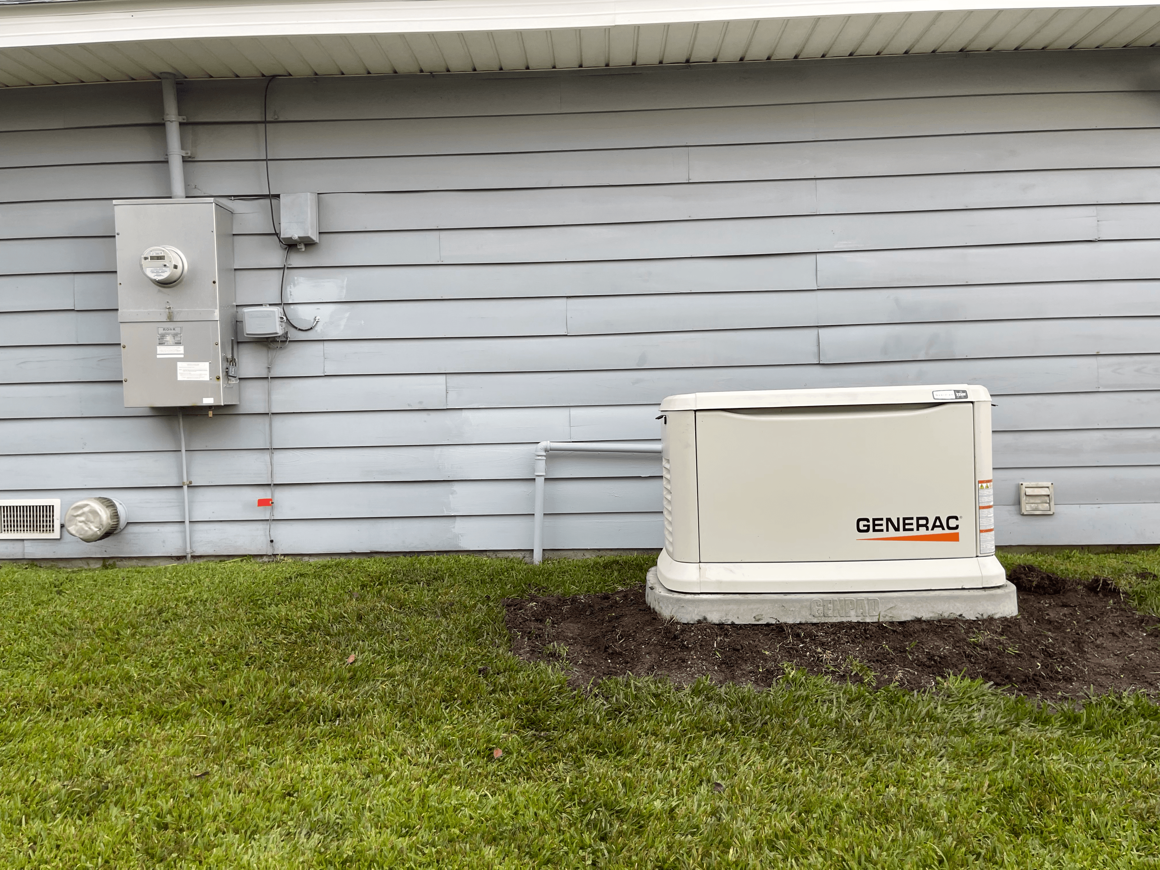 Generac standby generator on a concrete pad next to a house with light gray siding.