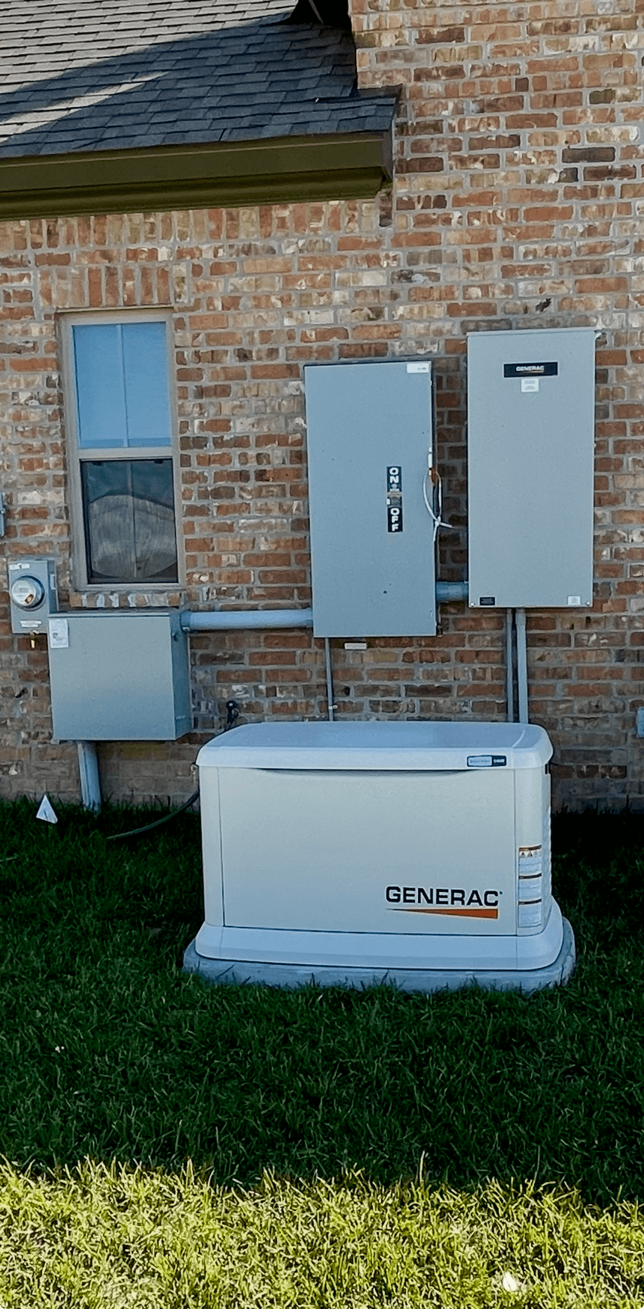 Generac standby generator installed on a lawn against a brick wall with electrical panels.